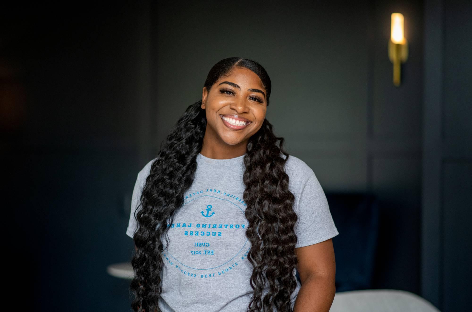 Photo of  FLS Participant Elaina  ( female,  gray t-shit blue lettering,  in a office background)